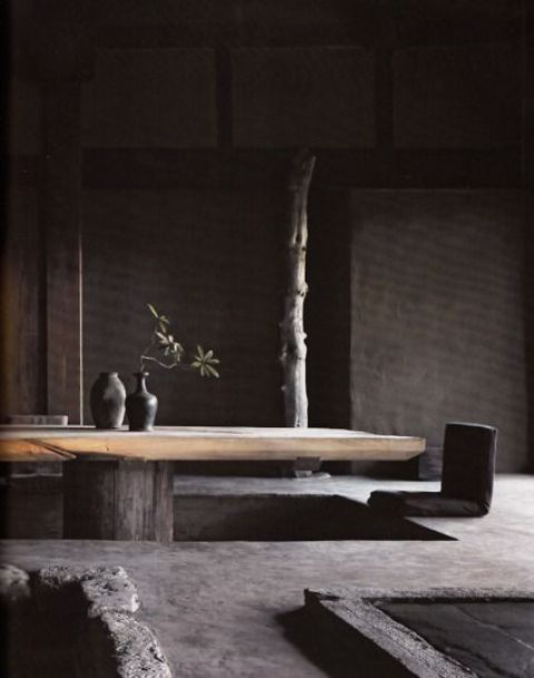 a wabi sabi living room with rough stone walls, floor and a rough wooden low table is pretty moody
