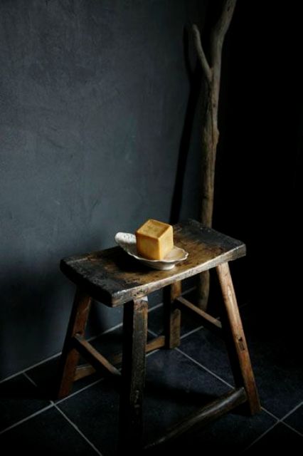 a simple matte black wall of painted concrete, a burnt wooden stool and a wooden stick for a natural and wabi sabi look