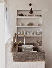 a wabi-sabi kitchen with rough white concrete walls, built-in shelving and a stone sink looks unusual and cozy