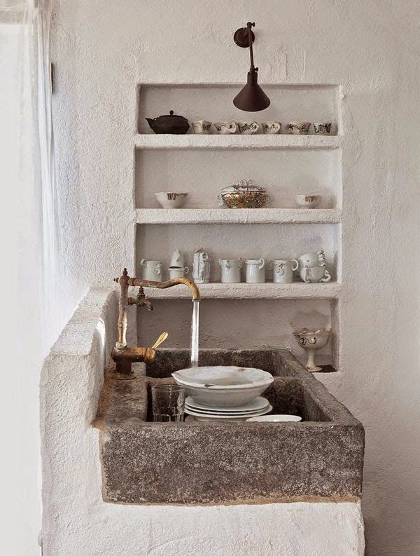 a wabi sabi kitchen with rough white concrete walls, built in shelving and a stone sink looks unusual and cozy