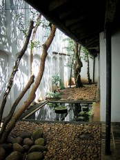 a beautiful and chic courtyard with pebbles, a couple of trees and greenery, rocks and a pong with a stone bowl in the center