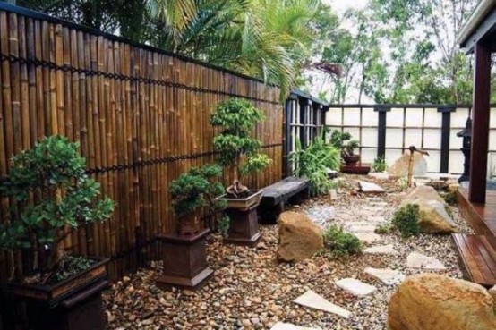 a Japanese rock garden with large rocks, mini trees in pots, a stone bench and a fountain