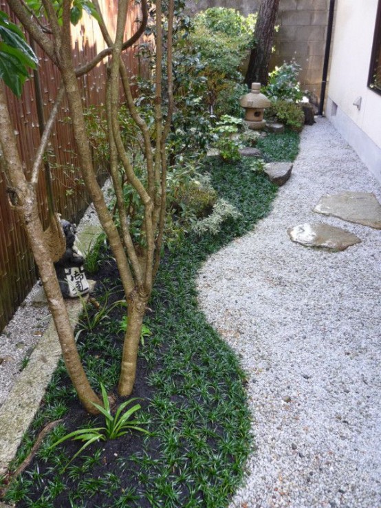 un jardín japonés con césped, guijarros, vegetación, árboles bajos y faroles de piedra, además de rocas planas