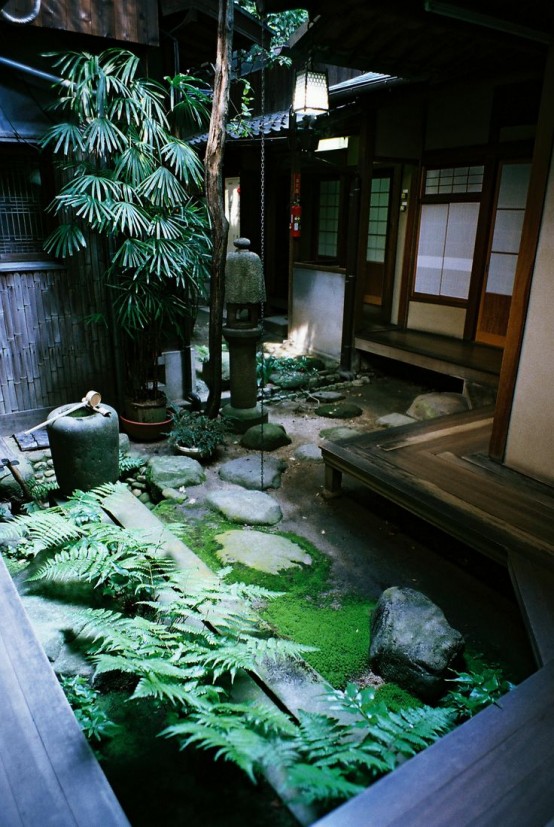 a Japanese backyard with moss, ferns, rocks, stone lanterns and a low tree for a calming and welcoming space