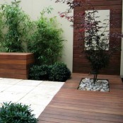 a contemporary wooden deck with a single tree with pebbles, greenery and a wooden wall