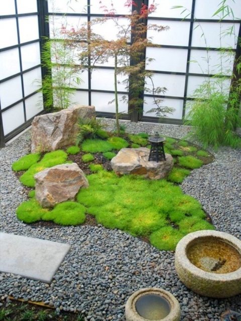 un patio japonés con guijarros, rocas, cuencos de piedra, una linterna y vegetación alrededor