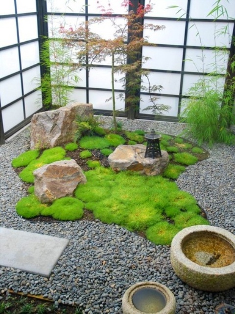 a Japanese courtyard with pebbles, rocks, stone bowls, a lantern and greenery around