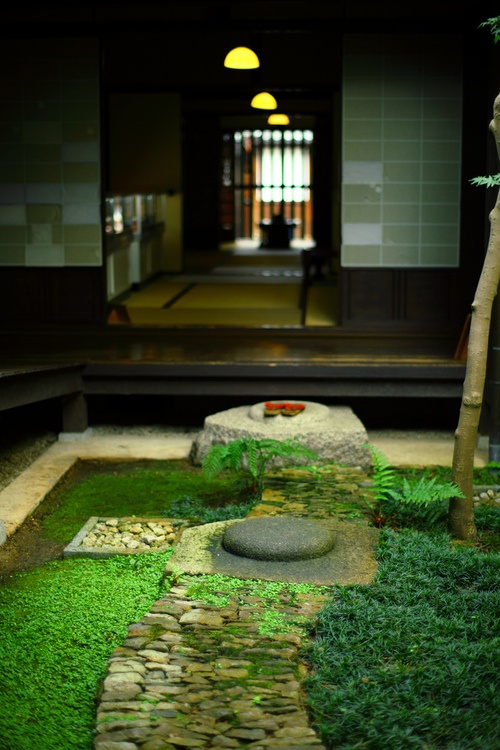 a Japanese garden with greenery and moss, rocks and pebbles and some bamboo