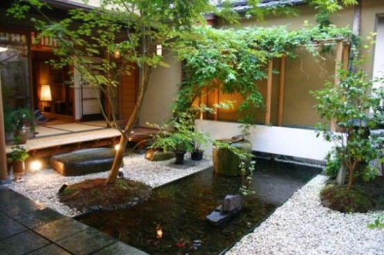 un hermoso patio trasero japonés con un espacio cubierto de piedra, un estanque en el centro y rocas y árboles, además de vegetación