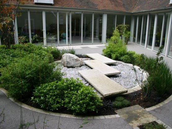 un patio trasero de inspiración japonesa con mucha vegetación, un jardín de rocas y baldosas de piedra encima