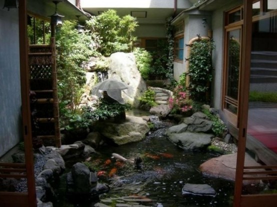 an amazing Japanese garden with a pond, a small waterfall, large rocks, greenery, a large Japanese lantern