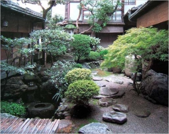 un relajante jardín japonés con guijarros, grandes rocas, un puente de madera, árboles, faroles y un estanque