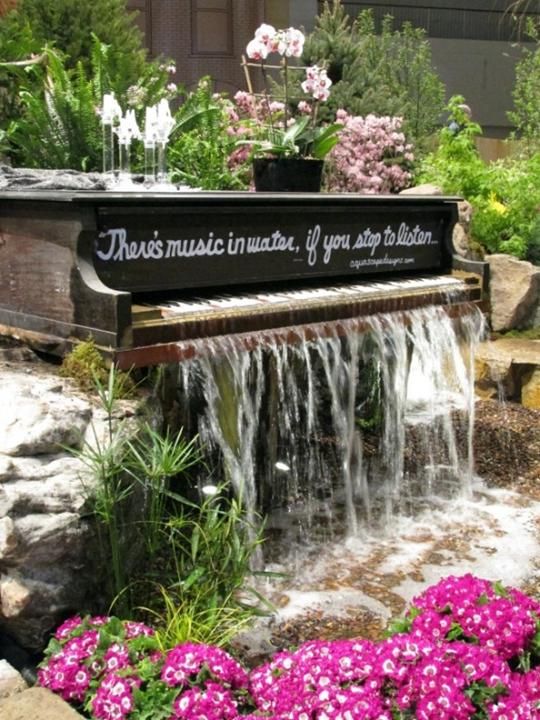 a lovely and creative piano fountain with pink blooms on top and around it is a great idea for music fans or for those who love something unique