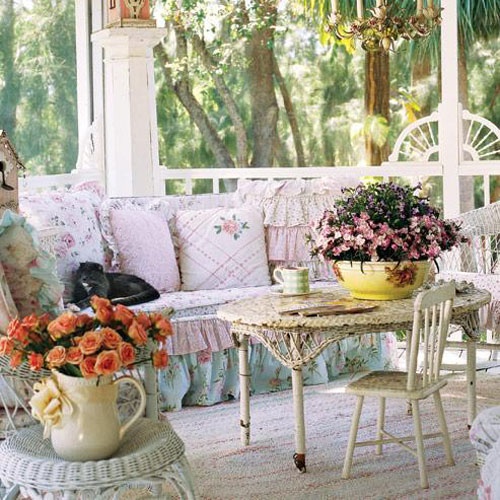 a shabby chic porch with elegant vintage furniture, cute floral pillows and potted greenery and flowers