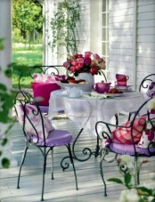 a cheerful summer porch with forged furniture, colorful cushions and pillows, tableware and greenery