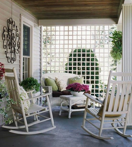 a simple vintage-inspired summer porch with white wicker furniture, bright pillows, potted greenery and blooms