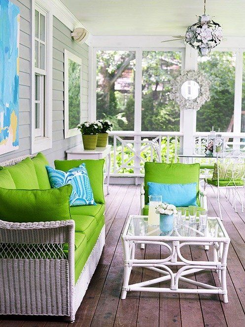 a bright and fresh summer porch with white wicker furniture, bright green and blue textiles and a white rattan coffee table