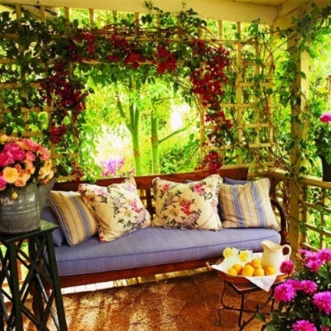 a colorufl summer porch with a ouch with bright pillows, a trellis with blooms and potted flowers and greenery