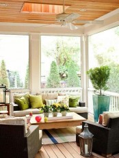 a modern summer porch with wicker furniture, bright pillows, candle lanterns and potted greenery and blooms