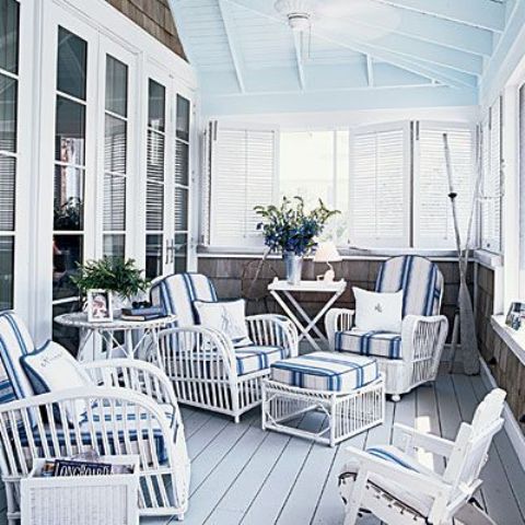 a coastal porch with white rattan furniture, striped navy and white upholstery, oars and shutters