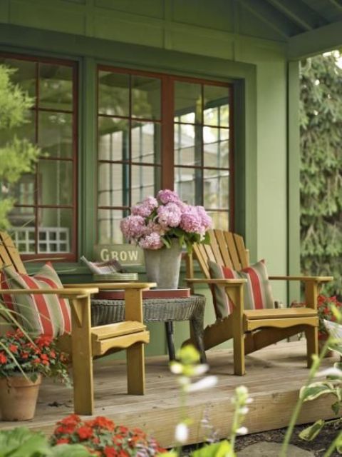 a welcoming rustic porch with wooden chairs and a wicker coffee table, potted blooms and a bucket with flowers