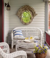 a summer porch with white wicker furniture, blooms in a basket, a shabby chic mirror and printed textiles