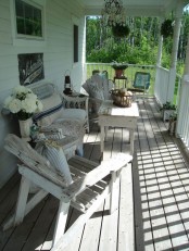a neutral and relaxed summer porch with shabby chic and weathered wooden furniture, wicker pieces and some greenery and blooms