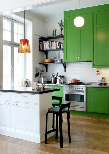 a chic kitchen in bold green, a white tile backsplash and a white ktichen island with black countertops