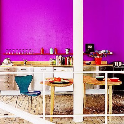 a vibrant kitchen with a hot pink wall, neutral cabinetry, wooden tables and a navy chair is a fantastic statement