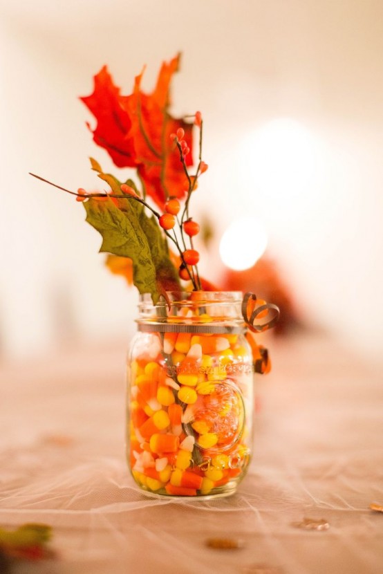 a jar filled with corn candies and with faux fall leaves, berries is a simple last minute centerpiece