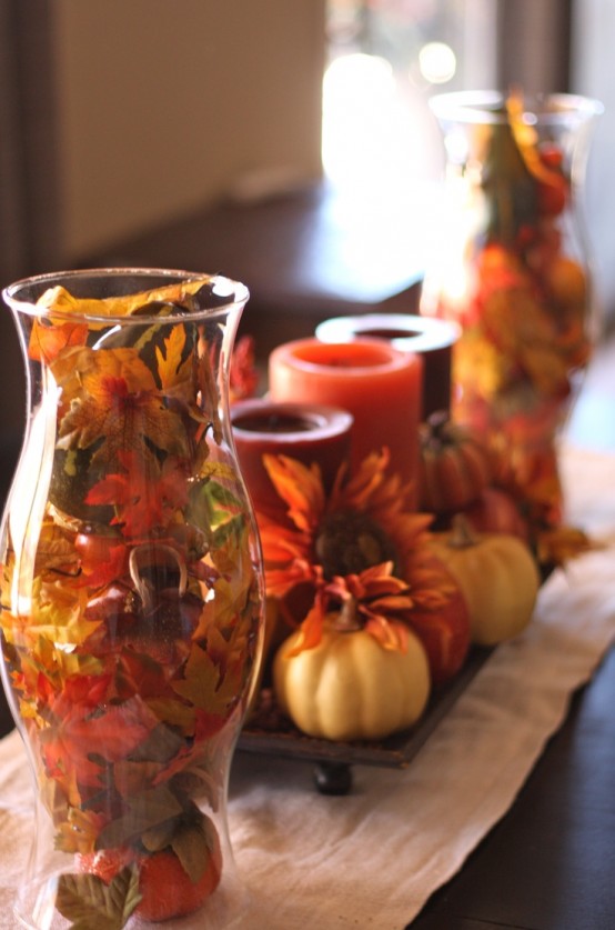 a clear vase with faux fall leaves and berries plus a stand with faux blooms, pumpkins and fall-colored candles