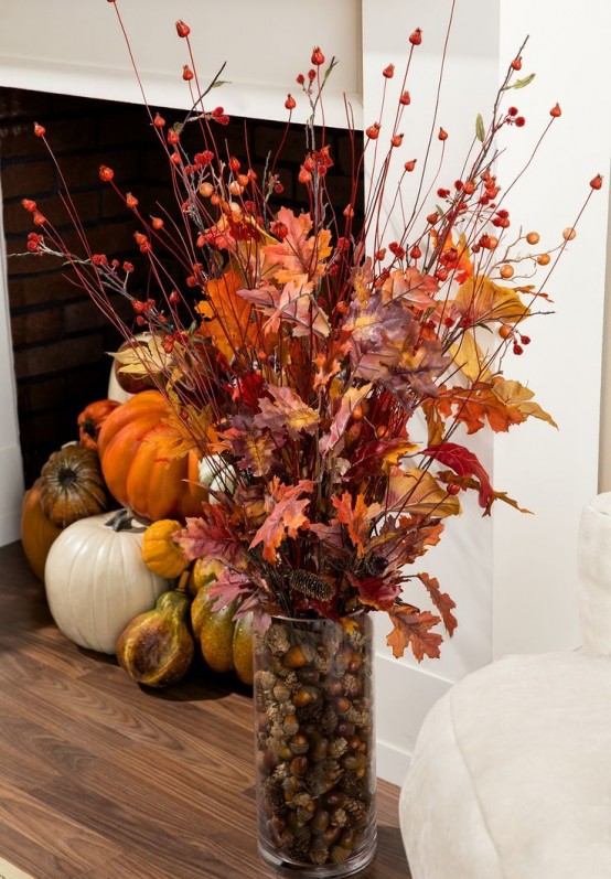 a clear vase with acorns and pinecones, fall leaves and berries and branches is a cool natural fall centerpiece