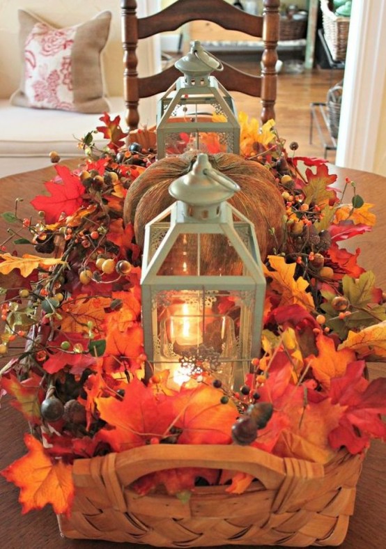 a basket centerpiece with fall leaves, berries, acorns, candle lanterns and a faux pumpkin is a cozy rustic centerpiece