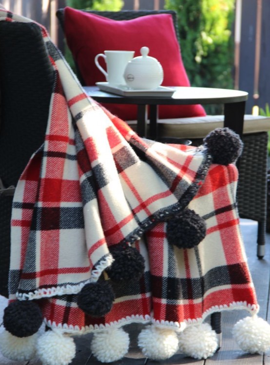 a plaid blanket accented with oversized pompoms is a cozy and cool piece to cover up on cold days