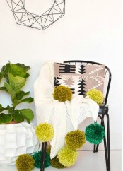 a white crochet blanket with oversized mustard and green pompoms that add color and fun to the piece