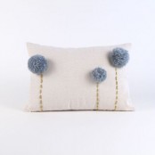 a neutral pillow with grey pompoms that accent it and imitate blooms is a cool and whimsy decoration for your space