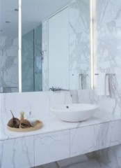 a minimalist bathroom done with white marble tiles and large lit up mirrors plus a vessel sink is chic