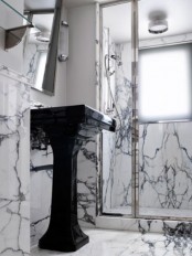 a tiny yet luxurious bathroom done with white and black marble, with a shower space and a black free-standing sink
