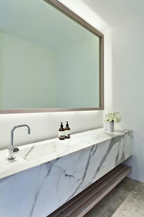 a minimalist bathroom with white walls, a large mirror, a floating marble vanity and a wooden shelf