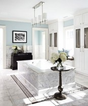 an elegant white marble and light blue bathroom with a marble clad tub and dark touches for a more dramatic look