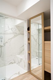 a minimalist bathroom done with white marble in the shower zone and a large sleek closet of wood to store everything