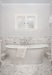 a vintage bathroom done in white and with white marble tiles on the walls and floor plus an oval tub