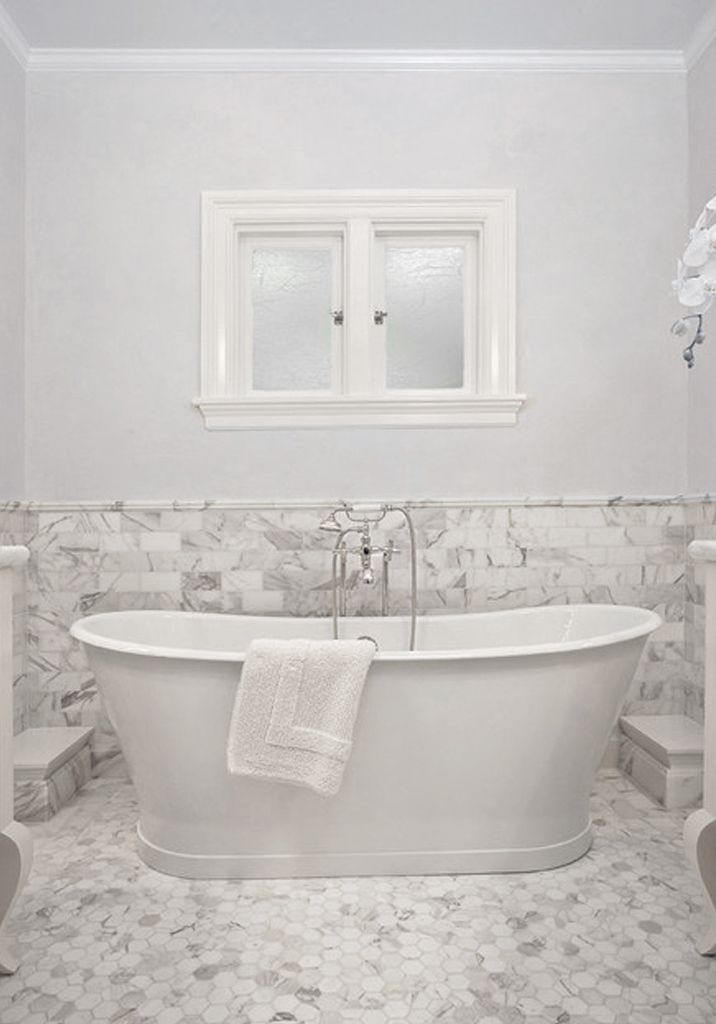a vintage bathroom done in white and with white marble tiles on the walls and floor plus an oval tub