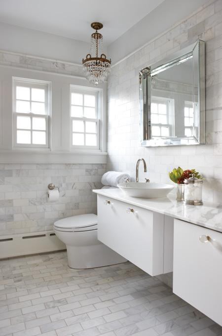 a glam white bathroom done with a floatign vanity, white marble tiles and a crystal chandelier