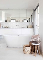 an eclectic bathroom featuring an oval tub, marble tiles and shiny ones on the wall, a floating vanity and mirror cabinets