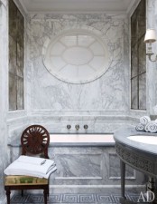 a gorgeous vintage grey marble bathroom with a tub, a sink on a stand and a round frosted glass window