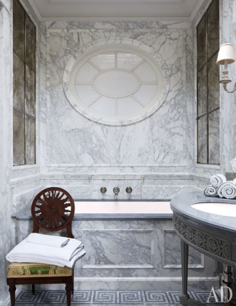 a gorgeous vintage grey marble bathroom with a tub, a sink on a stand and a round frosted glass window