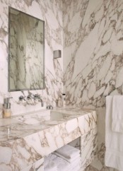 a chic white marble bathroom with marble covering and cladding everything plus a mirror