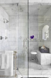 an elegant bathroom done with white marble tiles and a matching tile floor plus a marble bench in the shower space