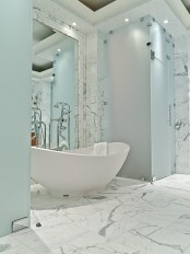 a chic bathroom all done with white marble, a mirror wall and touches of blue frosted glass